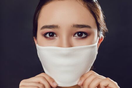 Asian girl in a face protective mask against coronavirus on a black background.の写真素材
