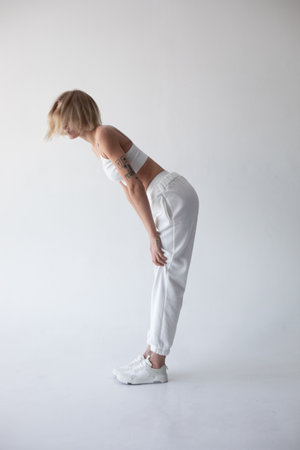 Beautiful blonde girl in a white top and tights posing on a white backgroundの写真素材