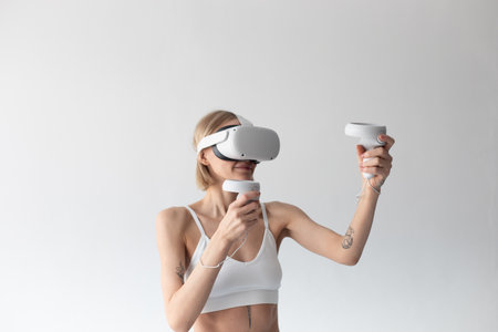 Beautiful thin girl in white shorts and a top in a virtual reality helmet posing on a white backgroundの写真素材