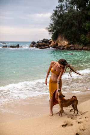 A Young Woman Happily Enjoying a Relaxing Beach Walk with Her Dog by the Ocean Wavesの写真素材