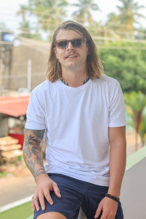 A man in sunglasses and a white tshirt stands on a balcony