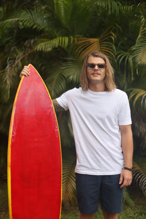 A surfer is depicted riding a red board amidst a vibrant tropical setting, basking in the sunの写真素材