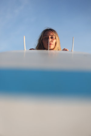 A woman is joyfully surfing at sunset with her surfboard against a clear blue skyの写真素材