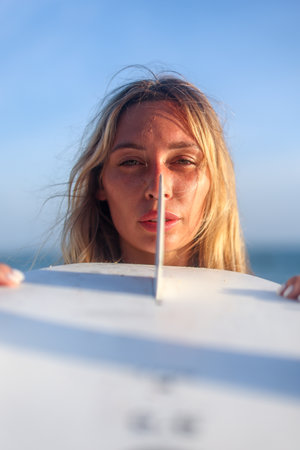 A woman is joyfully surfing at sunset with her surfboard against a clear blue sky