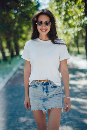 Happy Young Woman In White T-Shirt And Denim Skirt Walking In Parkの写真素材