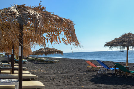 Beach umbrellas and sun loungers on the black sand of the beachの写真素材