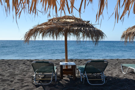 Chairs and umbrella on the black sand beach on the background of the seaの写真素材