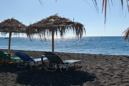 Beach umbrellas and deckchairs on the black sand of the island of Creteの写真素材