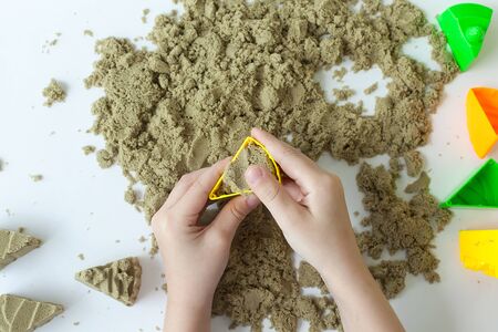 happy Girl plays kinetic sand in quarantine. Blond beautiful girl smiles and plays with purple sand on a white tableの写真素材