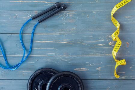 Dumbbell with notebook, scales, jumping rope and bottle of water on wooden backgroundの写真素材