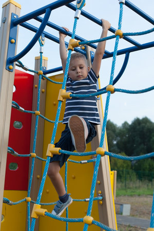 a little boy on the Playground, hanging on a rope ladder. Games on fresh air.