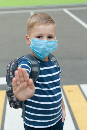 A small schoolboy in a mask during an outbreak of the corona virus and flu.Mask for prevention of coronavirus. A little boy breathes through a mask while going to school.の写真素材