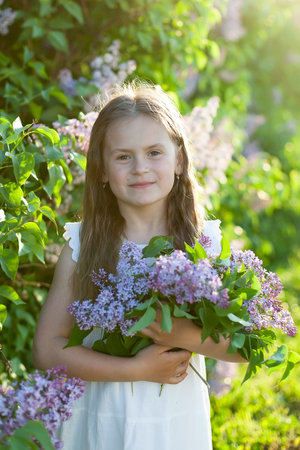 Young spring girl in spring garden. Young lady feeling happy in nature. Facial portrait of funny teenager girl. Girl with bouquet of lilacの写真素材