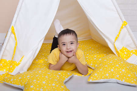 Portrait of a cute boy with Down syndrome sitting in a yellow hut.の写真素材