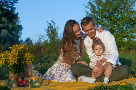 stylish young family of mom, dad and daughter, outdoors outside the city in the park among the trees in the summer.の写真素材