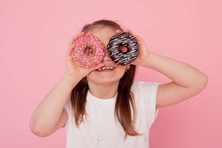 excited blond girl old holding two donuts on her eyes looking through them playing cheerful in sugar calories and unhealthy sweet nutrition abuse addictionの写真素材