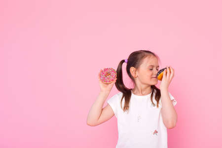 Studio portrait of a beautiful little girl holding a donut and smelling tasty flavor. Isolated on pink backgroundの写真素材