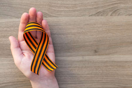 orange and black striped ribbon symbol on May 9 in hands isolated on white background. Victory Day