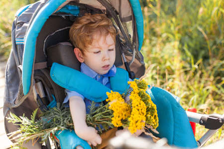 Child sitting on wheelchair is enjoying activities in the park like other people. Happy disabled kid...