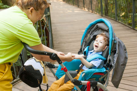 A disabled boy in a wheelchair with his mother on the street on a summer day. Maternal love and...