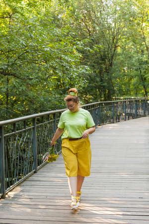 A young pretty woman in fashionable shorts and a T-shirt with a bouquet of wild flowers in her hands is walking in the park on a summer day. Model plus size.の写真素材
