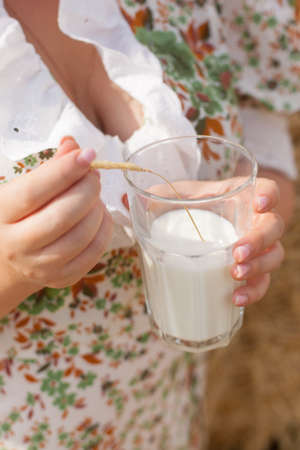a woman holds a glass of milk in her hand, useful habits, summer walks in a wheat field.の写真素材