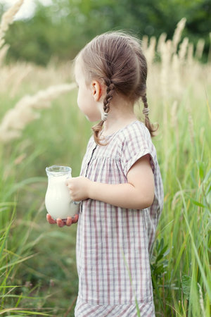cute little girl with a jug of milk in the field on a summer day, happy childhood.の写真素材