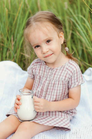 cute happy little girl in the wheat field holding a jug with milkの写真素材