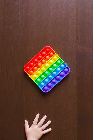 Child playing with rainbow pop it, pressing the bubbles with his fingers, top view.Image of clicks on the sidesNew antistress toy for children and adult.Copy space for text or design.の写真素材