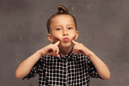 close-up portrait of a small beautiful girl with blonde hair pulled up in a bun. The child plays and poses. Childrens gamesの写真素材