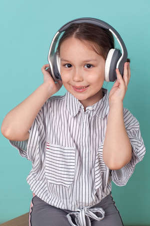 a little cute girl listens to music with large headphones on a blue backgroundの写真素材