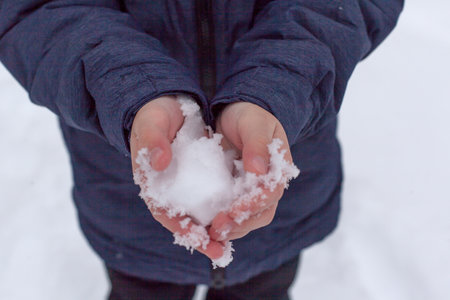 Holding natural soft white snow in his hand, outdoors. Winter day and snow in the hand. Sun glare is reflected in the snow. Hand holds cold snow. Spending time outdoors in winterの写真素材