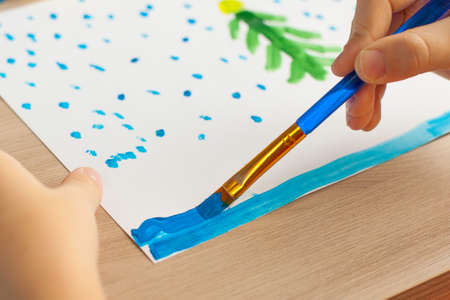 Childrens hands of a girl dip a brush in paint. In the background there are brushes, paints and New...