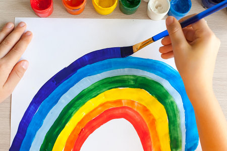 Kids painting watercolor rainbows at table at home. Arts and craftsの写真素材