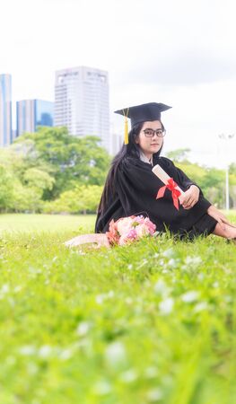 Beautiful asian women graduating holding diploma with pride and smiling in an academic gown.Congratulation happiness female student wearing graduation hat and gown ,background is nature in university.の写真素材