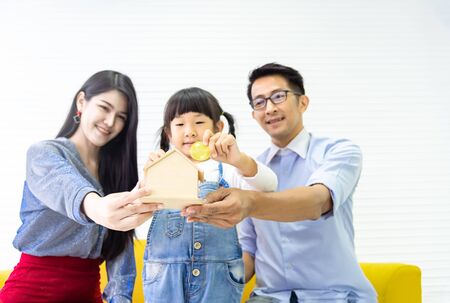 Hands holding piggy bank .Family saving money to wooden home bank. Pretty little girl and family putting coins into bank for dream house. Children, money, investments and people conceptの写真素材