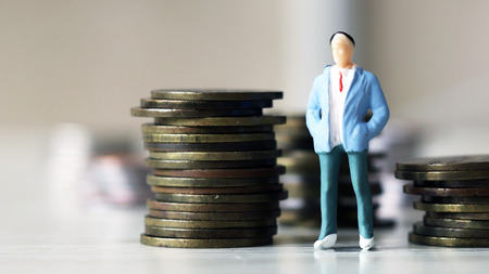 Concept of a savings plan. A miniature man standing next to a pile of coins.の写真素材