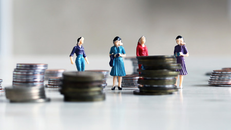 miniature of a working woman. A woman's miniaturization standing between piles of coinsの写真素材