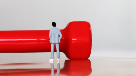 Adversity and humanity concepts. A miniature man standing in front of a big dumbbell.の写真素材