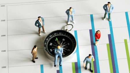 Miniature people and organizational concepts. Miniature people clustered around the compass