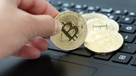 Hand holding the bitcoin on the keyboard.