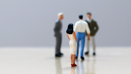 Men and women of miniature. The back of a woman looking at a group of men.の写真素材