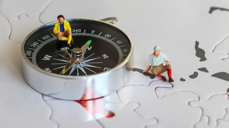 Two miniature tourists sitting on a compass.の写真素材