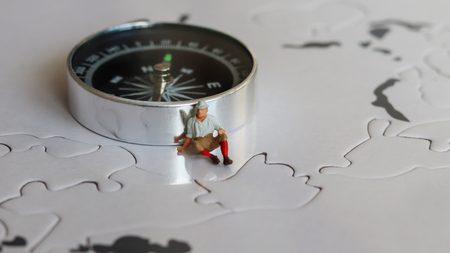Miniature man sitting beside a compass.の写真素材