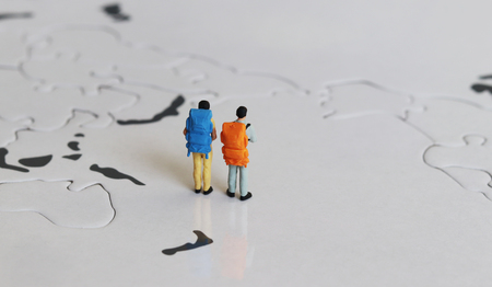 Two miniature tourists standing on a world map with a rucksack.の写真素材