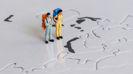 Two miniature tourists standing on a world map with a backpack.の写真素材
