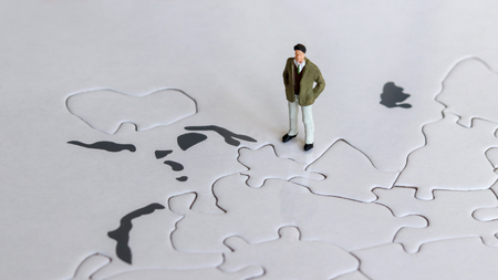 A miniature man standing on a world map.の写真素材