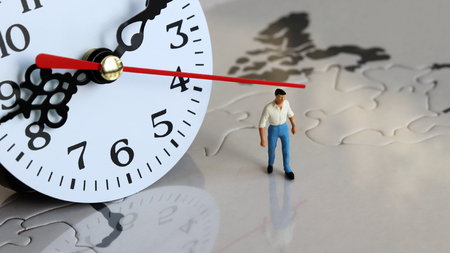 A miniature man standing in front of a clock.