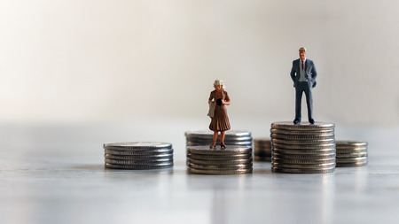Concept of gender discrimination in pay. A miniature standing on top of a pile of coins.