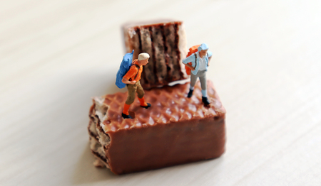 A miniature man and a miniature woman climbing a backpack on a chocolate.の写真素材
